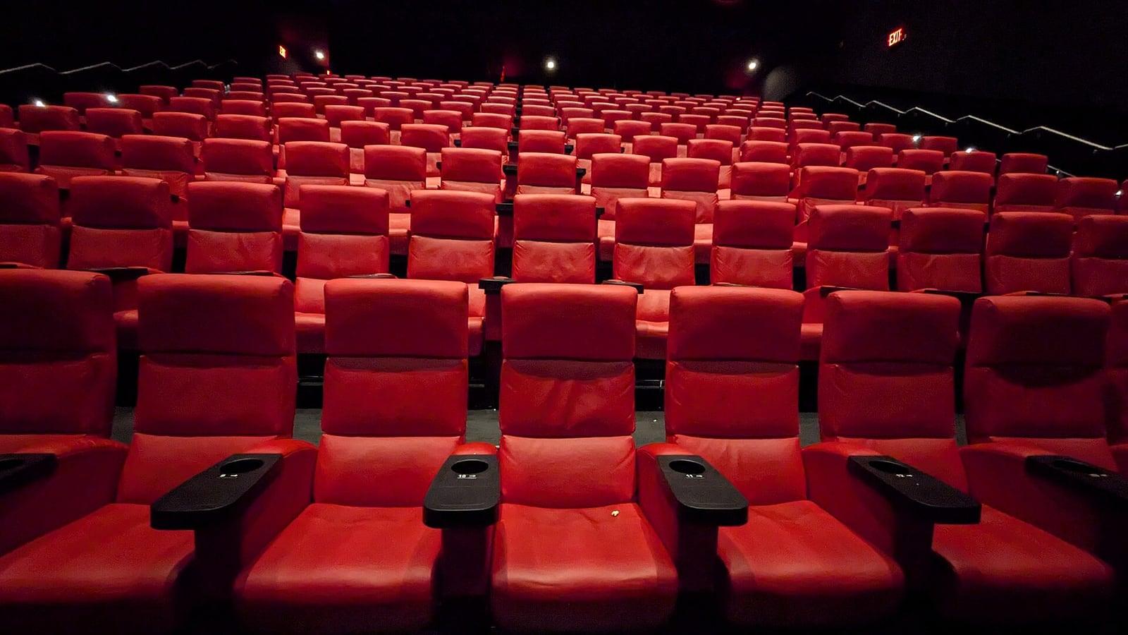 Rangées de fauteuils rouges vides dans une salle de cinéma plongée dans la pénombre