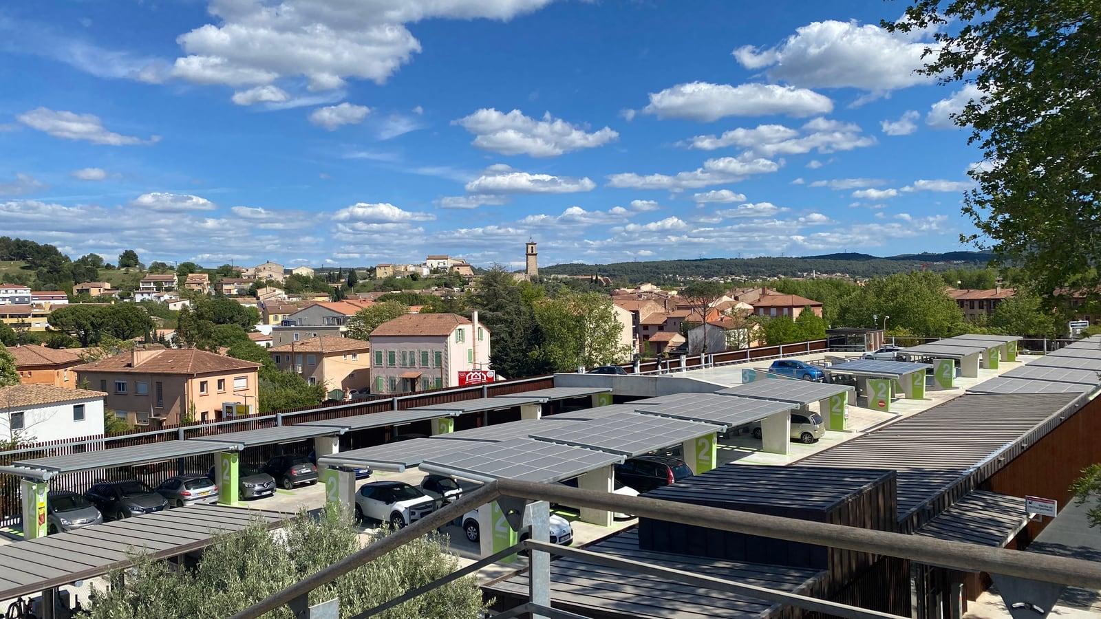 Vue sur les maisons et immeubles de Gardanne depuis le pont de la gare, avec le clocher au loin et, au premier plan, un parking couvert d'ombrières