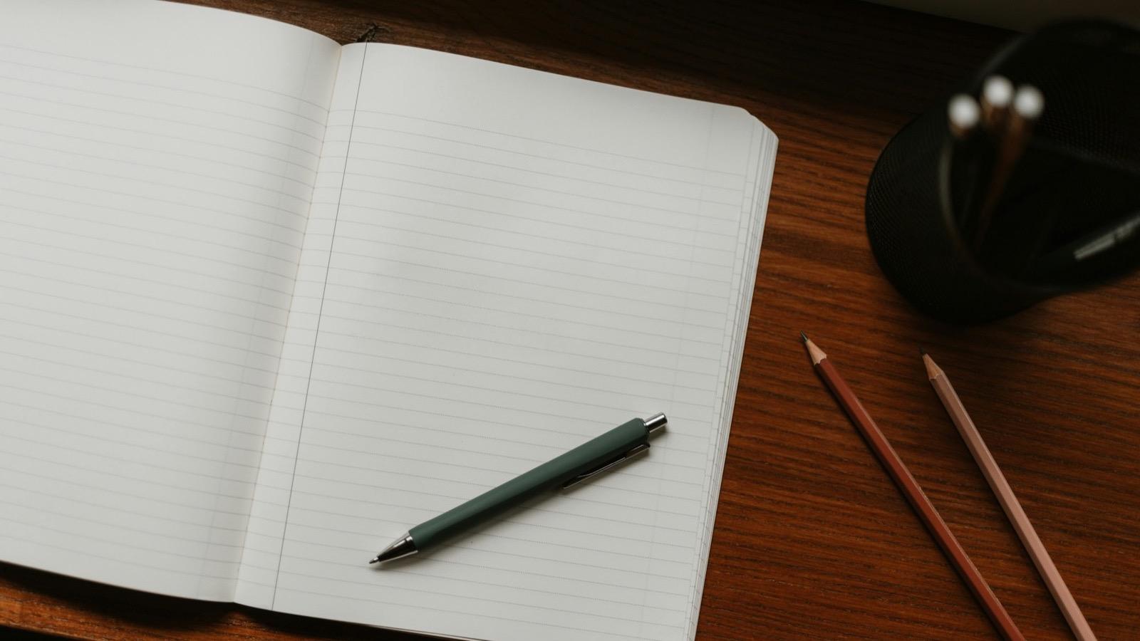 Un cahier ouvert, un stylo et des crayons sur un bureau (image d'illustration)