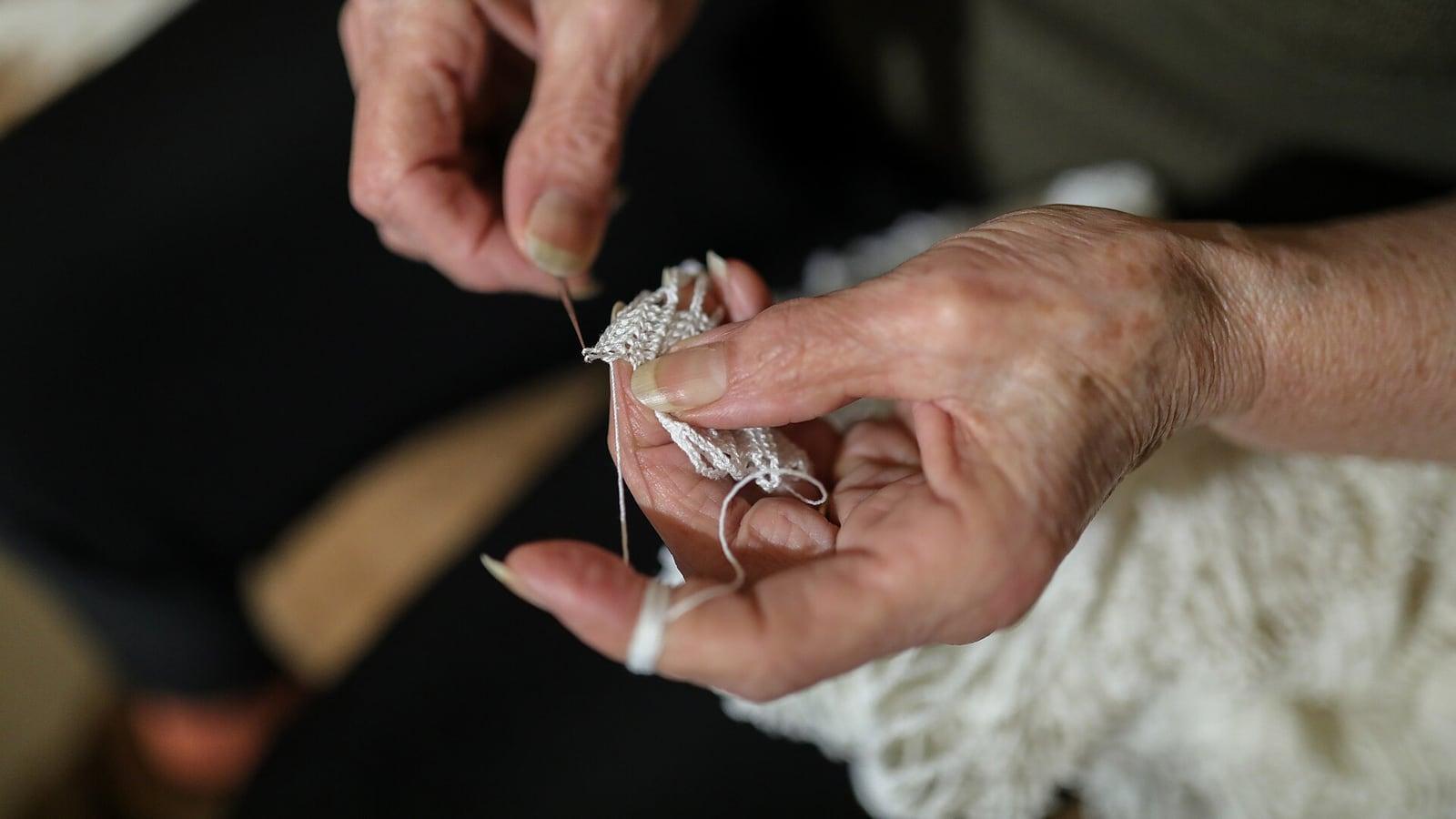 Gros plan sur les mains ridées d'une femme âgée qui fait du crochet avec un fil blanc