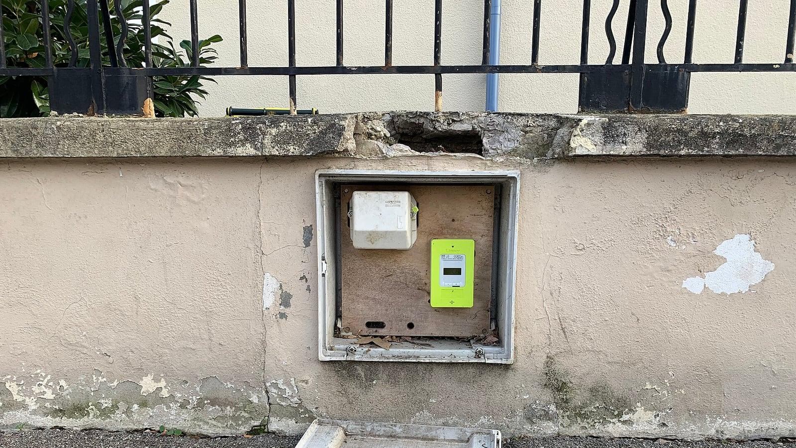 Un compteur électrique Linky vert dans un coffret ouvert, encastré dans un muret au bord d'un trottoir