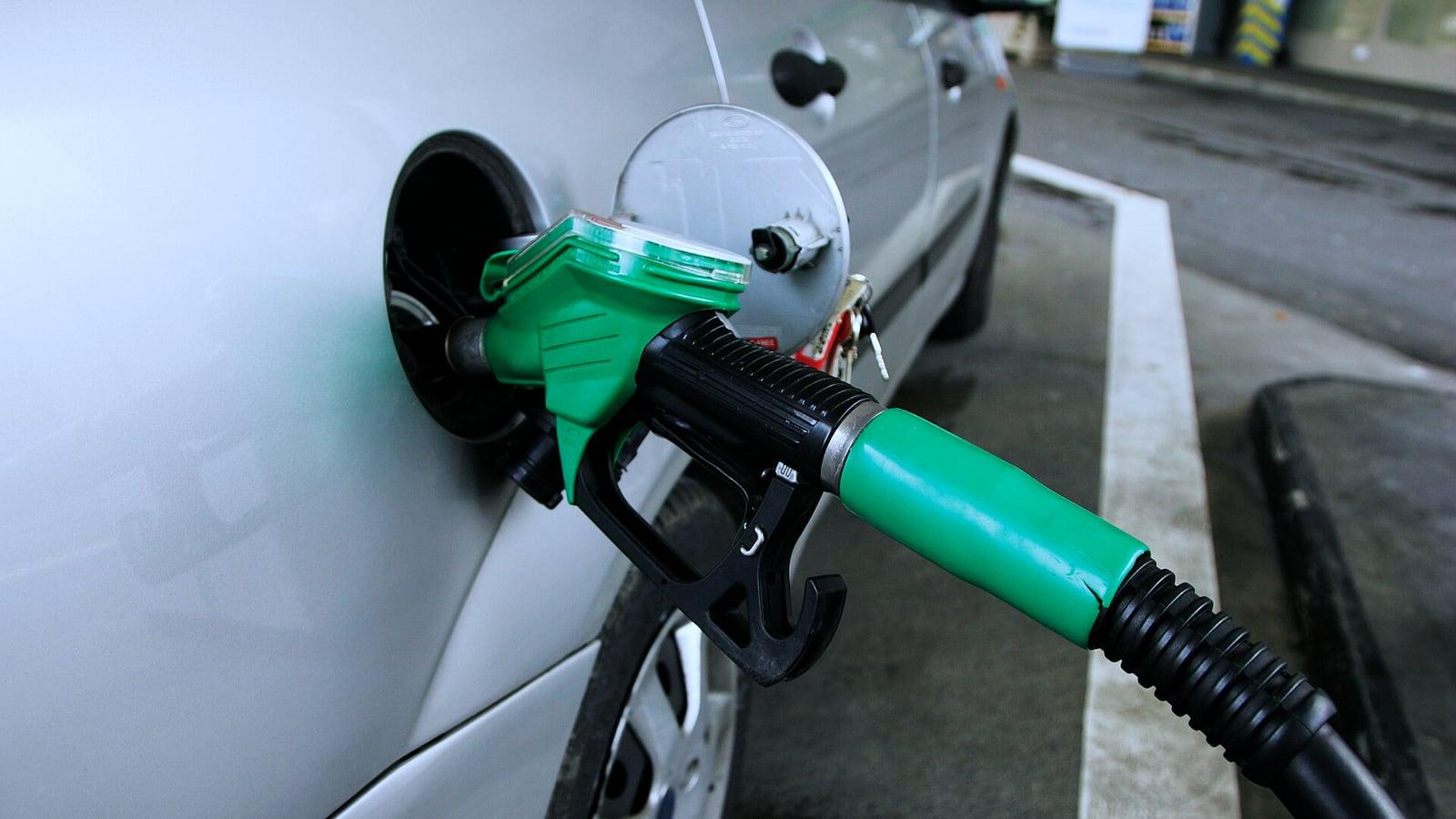 Un pistolet de pompe à carburant vert engagé dans le réservoir d'une voiture grise, dans une station-service