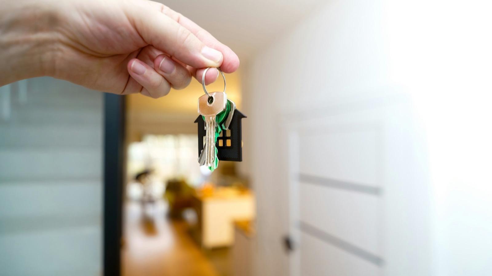 Une main tenant des clés de logement devant une porte d'entrée