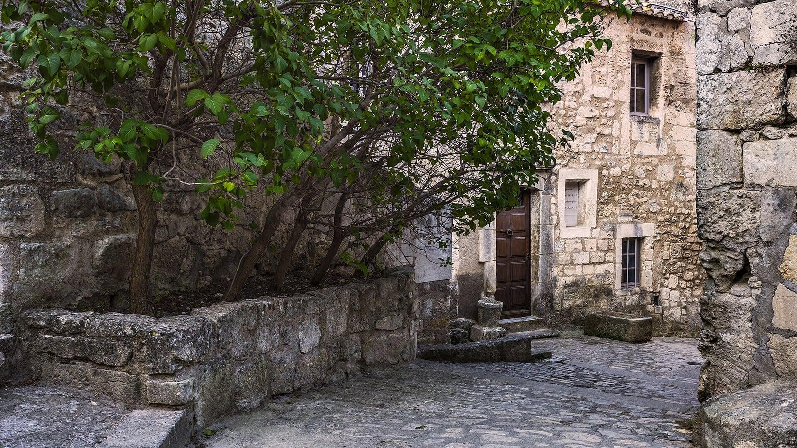 Une ruelle pavée bordée de maisons anciennes en pierre, avec une porte et des fenêtres de bois, aux Baux-de-Provence