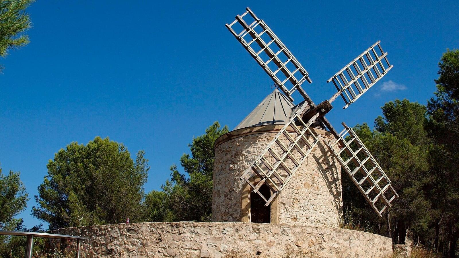 Le moulin à vent en pierre du chemin des Trois-Moulins à Gardanne, entouré de pins sous un ciel bleu