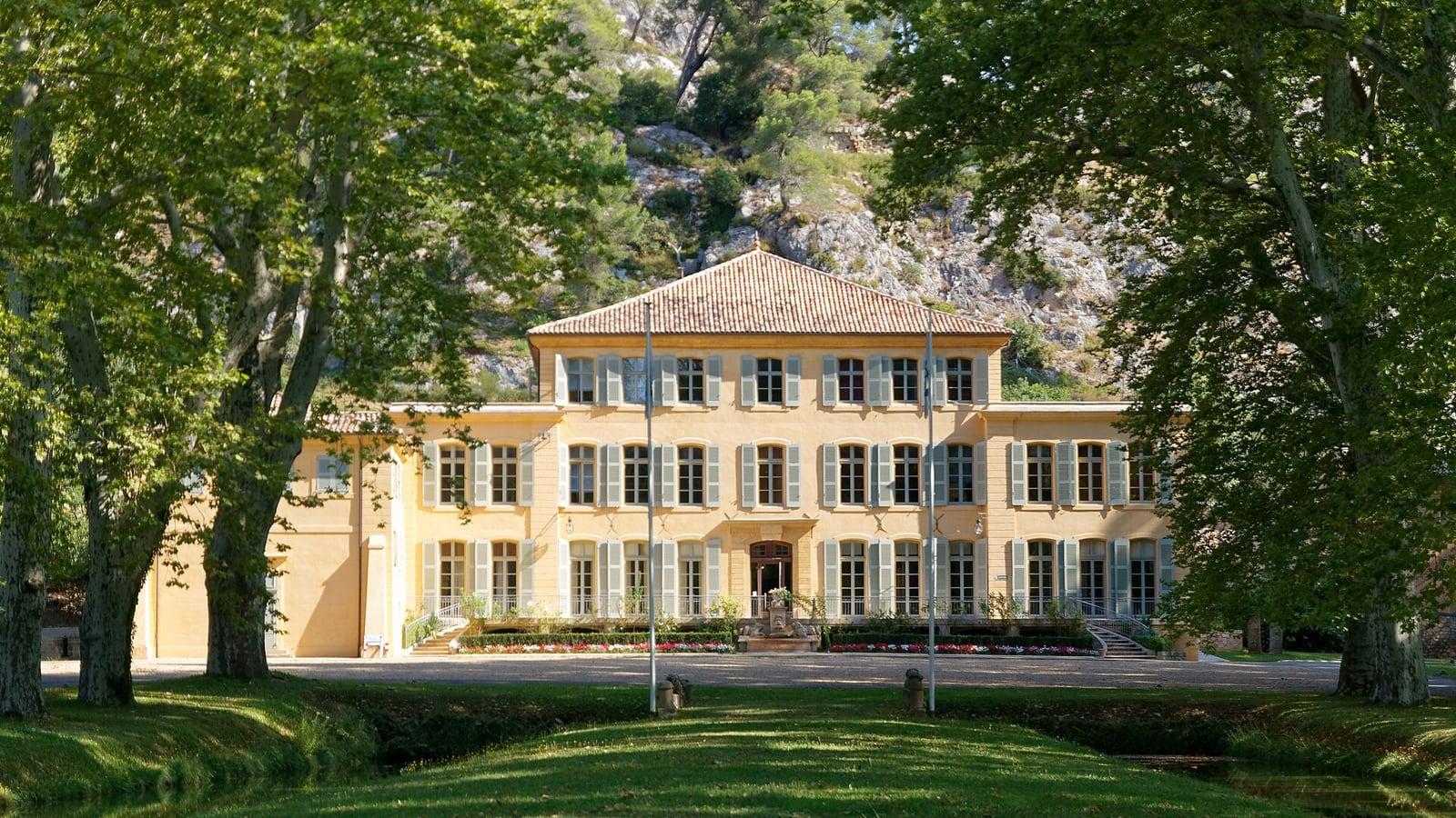 La façade ocre du château du Tholonet, aux volets gris, encadrée de grands platanes, au pied d'une colline rocheuse
