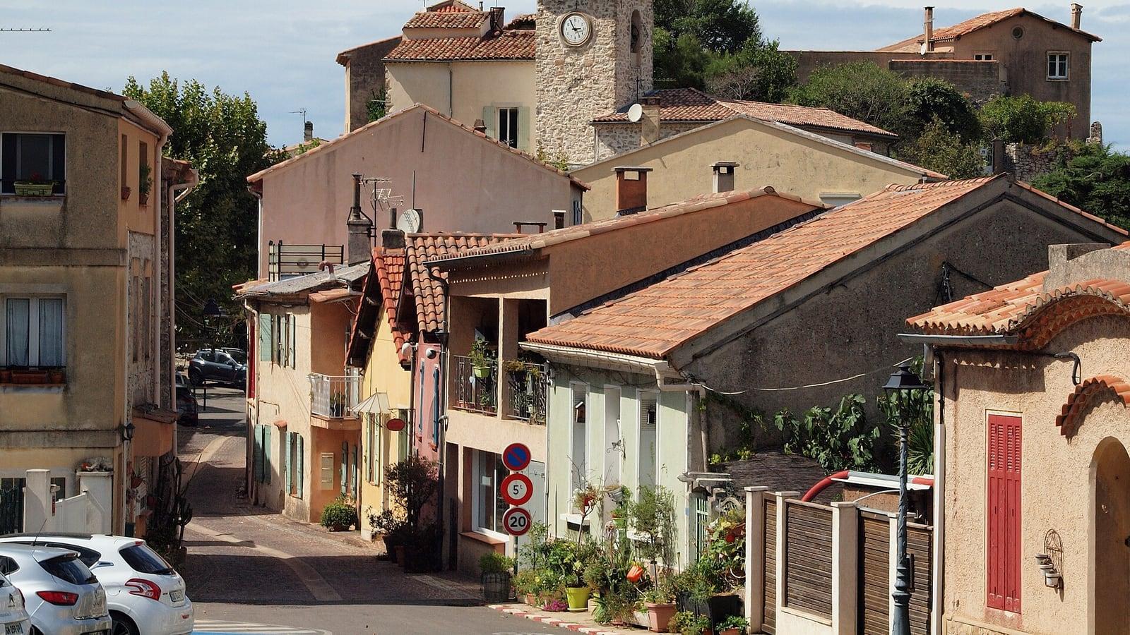 Maisons de village aux toits de tuiles et aux volets colorés le long d'une rue en pente à Mimet, sous un clocher à horloge