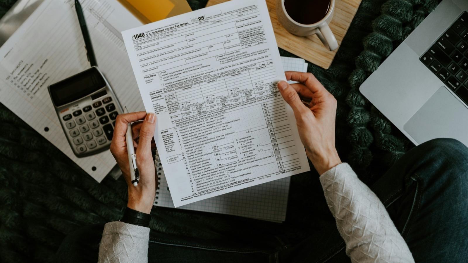 Des mains tenant des documents administratifs avec une calculatrice et un ordinateur portable