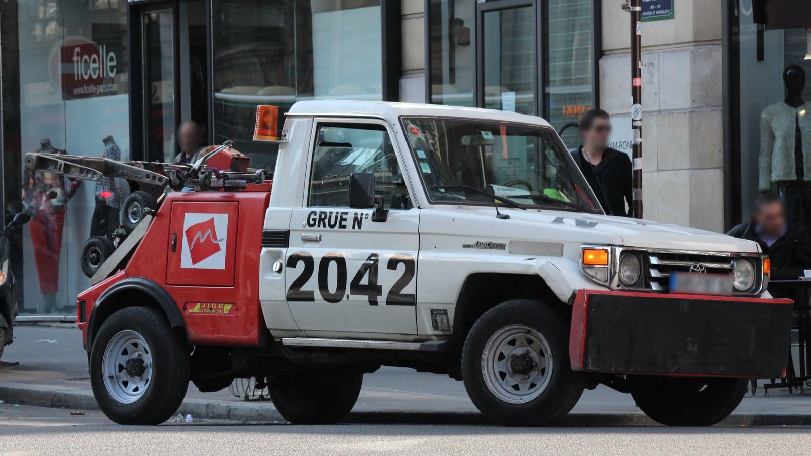 Une dépanneuse de fourrière rouge et blanche, marquée « Grue n° 2042 », stationnée dans une rue commerçante de Paris