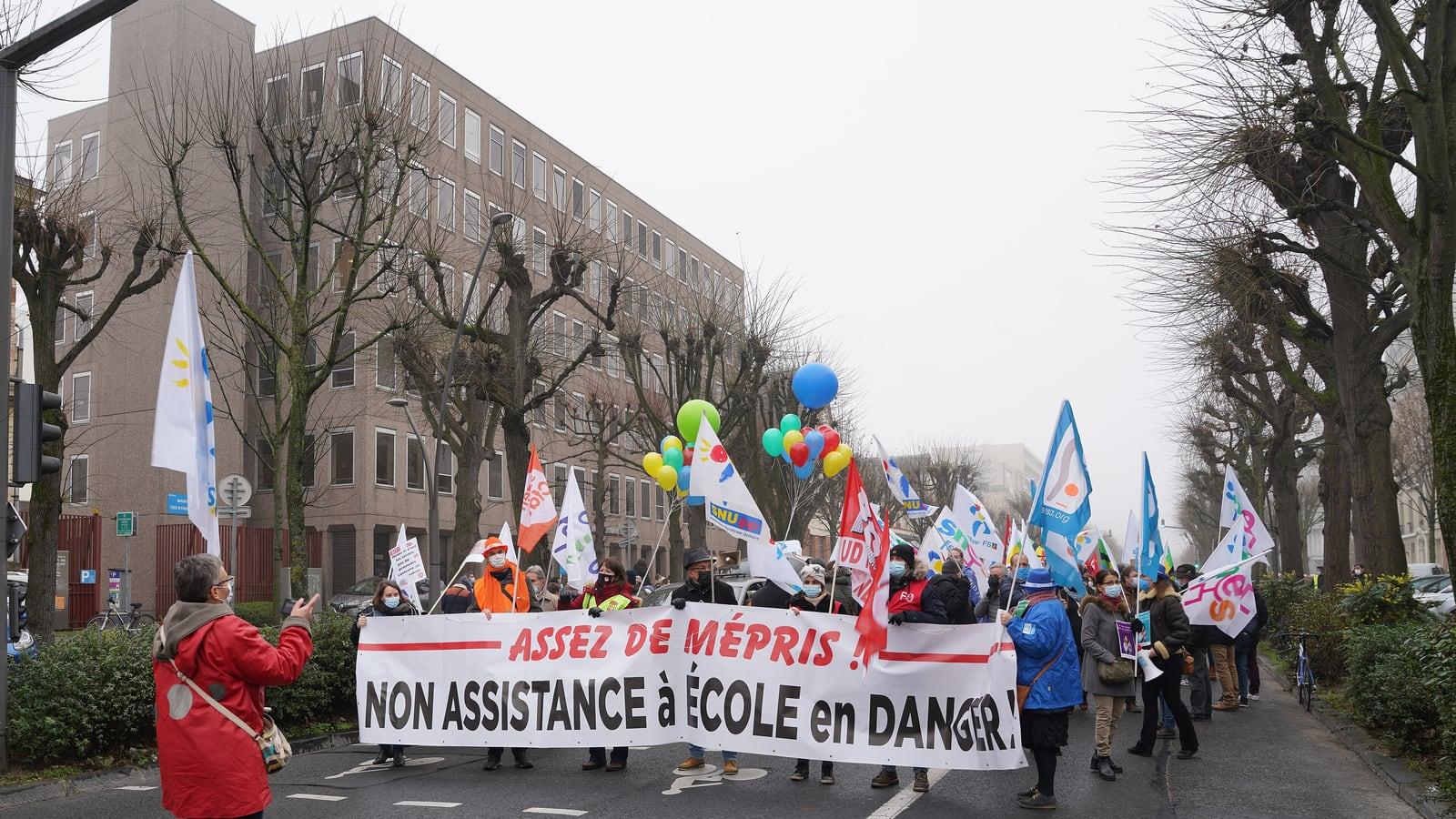 Un cortège d'enseignants en grève derrière une banderole « Non assistance à école en danger », avec drapeaux syndicaux et ballons