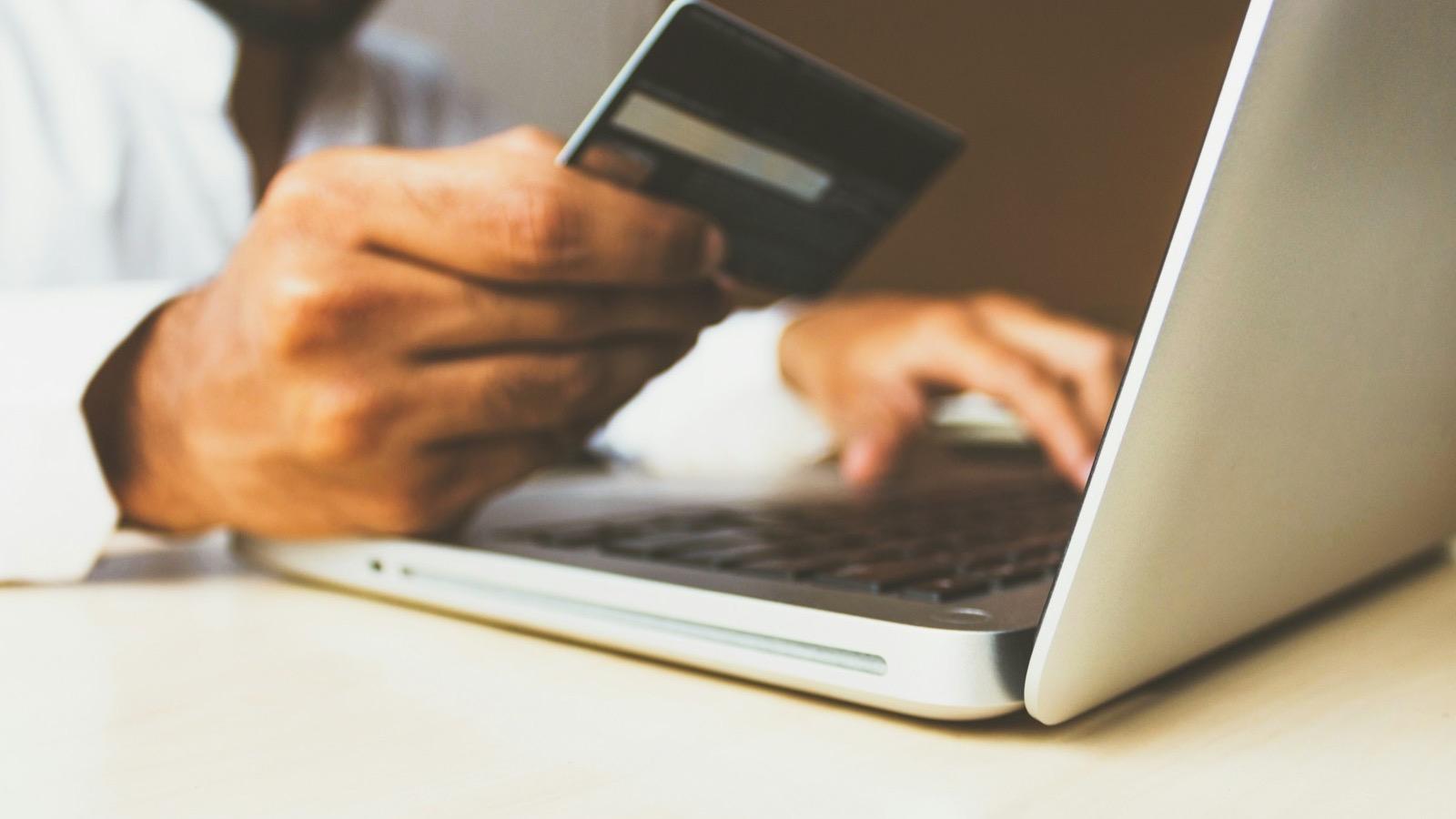 Une personne effectue un paiement en ligne avec une carte bancaire devant un ordinateur portable