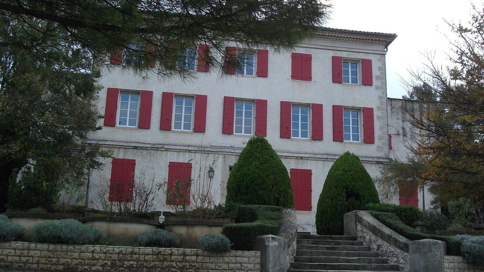 La façade aux volets rouges de l'hôtel de ville de Simiane-Collongue, précédée d'un escalier et de massifs taillés